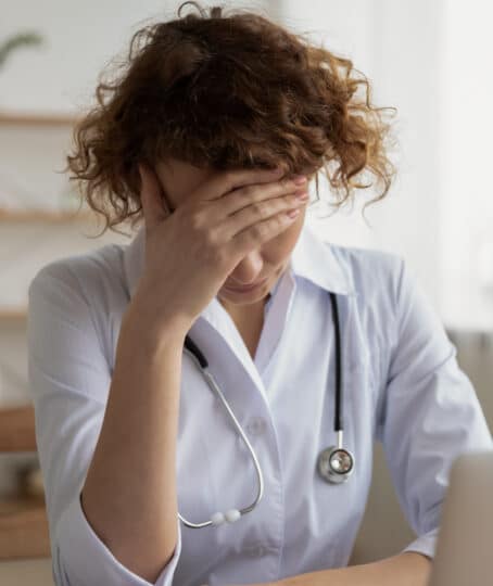 a female doctor sitting in front of a laptop looking tired and burnt out