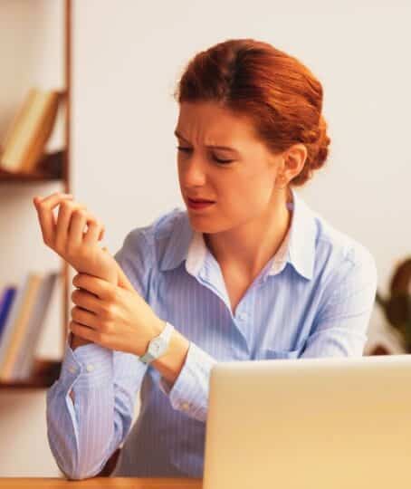 Businesswoman sitting at desk in office touch wrist feels pain. Unhealthy upset female having carpal tunnel syndrome because of active and long-term use of the keyboard and mouse in the wrong posture