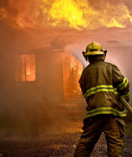 a lone firefighter with a hose putting out the blaze from a burning house