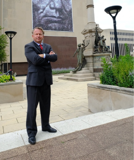 Todd Strong in suit with his arms crossed in a court yard