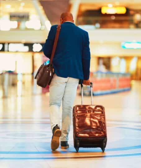 Suitcase, airport and black man travel for business opportunity, international career and immigration. Professional person or entrepreneur walking from behind with luggage for flight and global job