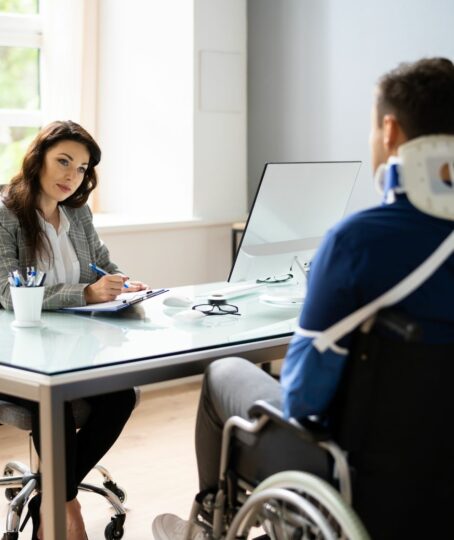 a lawyer talking to an injured worker with cast, neck brace, and sitting on a wheelchair