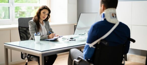 a lawyer talking to an injured worker with cast, neck brace, and sitting on a wheelchair