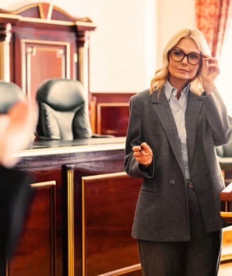 mature advocate pointing with hand and adjusting eyeglasses during questioning of witness in court