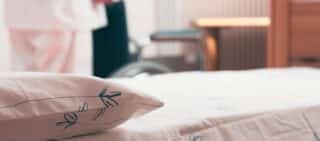 bed at nursing home with nurse and wheelchair on the background