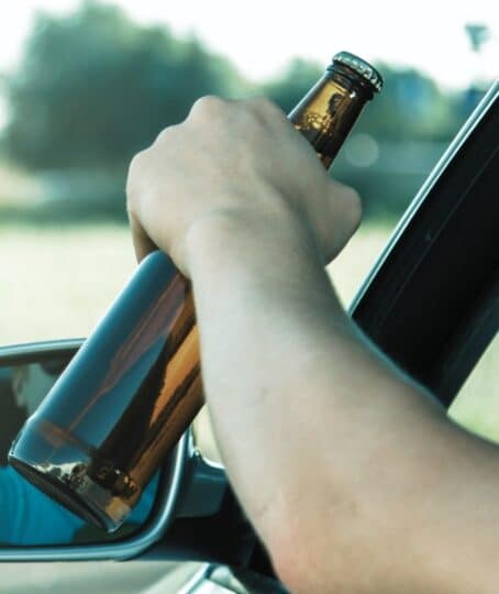 Car driver is holding a bottle of beer in his hand