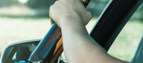 Car driver is holding a bottle of beer in his hand