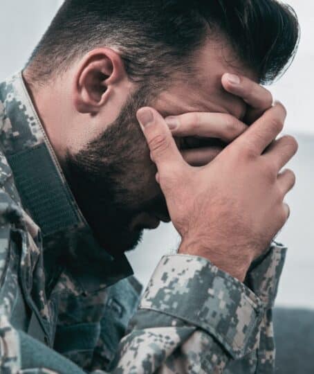 Side view of depressed army man in military uniform with post-traumatic stress disorder holding his head