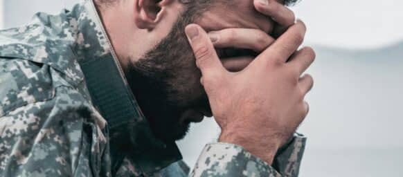 Side view of depressed army man in military uniform with post-traumatic stress disorder holding his head