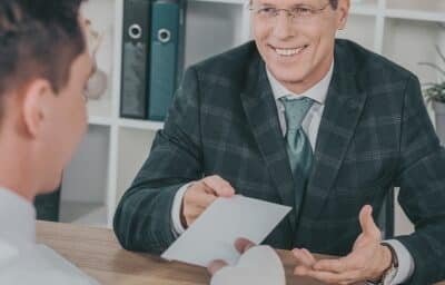 businessman in blue jacket taking paper from worker with broken arm. concept of lost wages