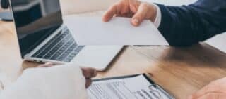 cropped view of businessman sitting at table and giving paper sheet to worker. Concept of is workers' comp taxable