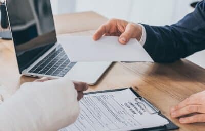 cropped view of businessman sitting at table and giving paper sheet to worker. Concept of is workers' comp taxable