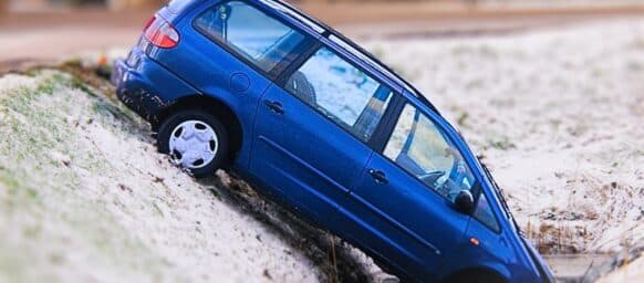 Blue mini van slides into watery ditch on a snowy winter road. Accidents due to poor road conditions