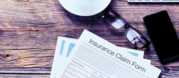 Insurance claim form. The form is on an old wooden table with a mobile phone, coffee, glasses and a keyboard. Third party insurance claim