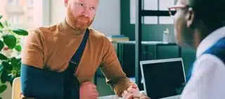 Man with hand in sling talking to insurance broker after workplace injury, how much do auto accident lawyers charge