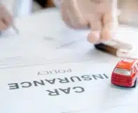 Car insurance policy with red car toy and blur image of man hand for vehicle insurance policy.