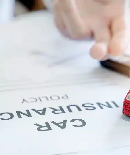 Car insurance policy with red car toy and blur image of man hand for vehicle insurance policy.
