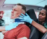 Paramedic placing a cervical collar to an injured man from car accident. Who pays for injuries in a car accident