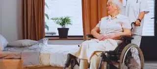 Nurse and an elder woman in a wheelchair inside a room in nursing home. Why Nursing Home Falls Are Still So Common