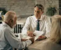 Man in a tie discussing documents with an older couple at a table.