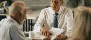 Man in a tie discussing documents with an older couple at a table.