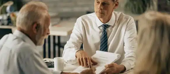 Man in a tie discussing documents with an older couple at a table.