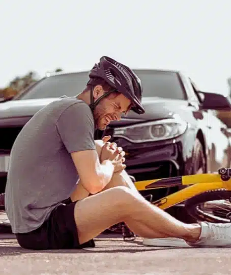 a man wearing a helmet sitting on the ground next to a yellow bicycle.