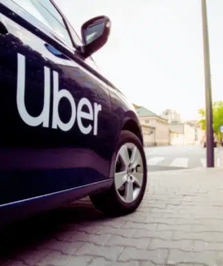 a close-up of a dark-colored car with the Uber logo prominently displayed on its side.