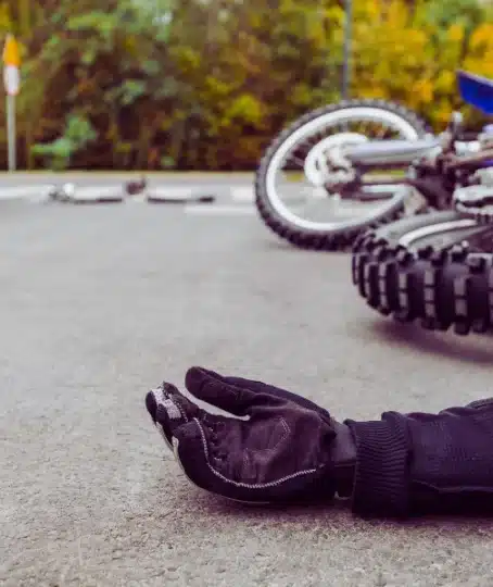 Aftermath of a severe car and motorcycle accident, with an injured person lying on the asphalt.