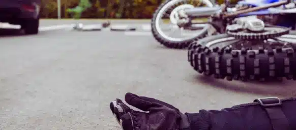 Aftermath of a severe car and motorcycle accident, with an injured person lying on the asphalt.