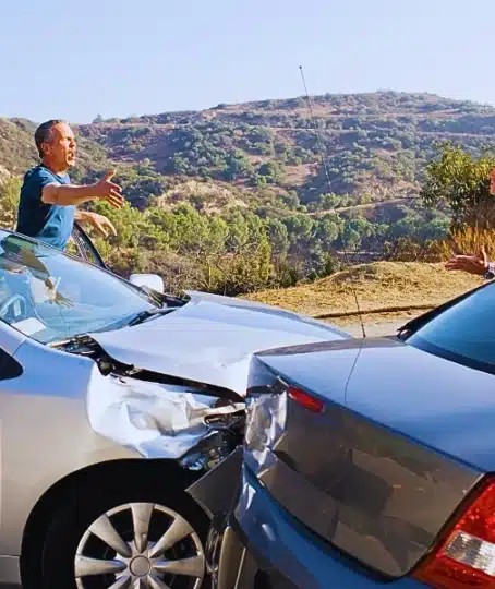 Two male drivers arguing on the side of a road immediately after a two-car traffic accident.