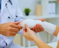 Doctor applying a white gauze bandage to patient's arm.