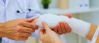 Doctor applying a white gauze bandage to patient's arm.