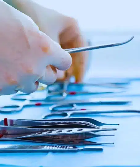 Gloved hands selecting stainless steel surgical instruments from tray.