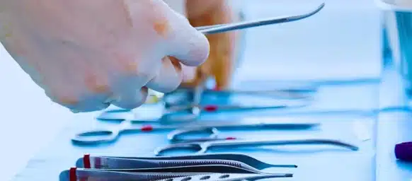 Gloved hands selecting stainless steel surgical instruments from tray.