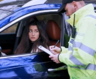 A woman in her car has been stopped by a police officer and is receiving a fine.