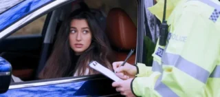 A woman in her car has been stopped by a police officer and is receiving a fine.