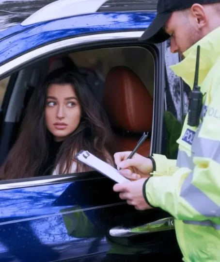 A woman in her car has been stopped by a police officer and is receiving a fine.