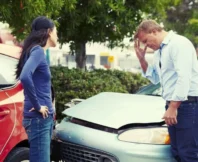 A man and a woman are standing outside their cars, looking dismayed and worried because they have just been in a car accident. changes their story after a car accident