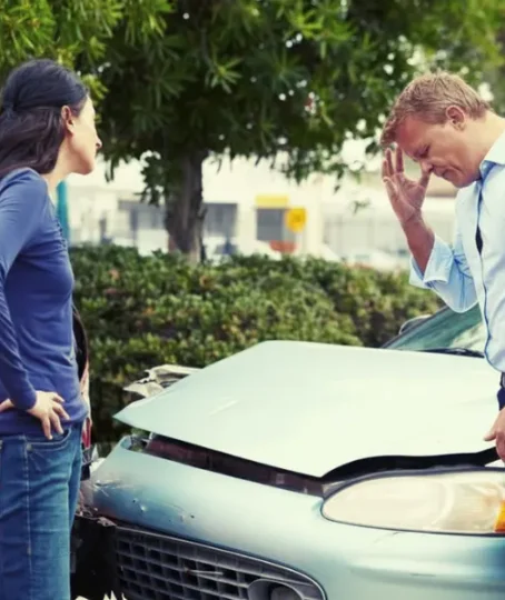 A man and a woman are standing outside their cars, looking dismayed and worried because they have just been in a car accident. changes their story after a car accident