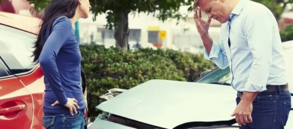 A man and a woman are standing outside their cars, looking dismayed and worried because they have just been in a car accident. changes their story after a car accident
