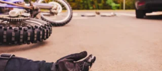 Accident on the highway involving a black car and a blue motorcycle. The motorcyclist is lying on the ground, showing his arm.