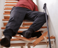 An elderly person fallen on a staircase next to broken wooden steps and a walking cane sue after falling on broken stairs