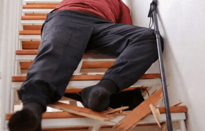 An elderly person fallen on a staircase next to broken wooden steps and a walking cane sue after falling on broken stairs
